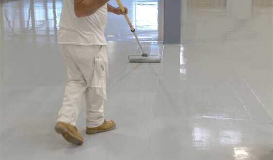 This image shows a man applying epoxy paint on an industrial floor.