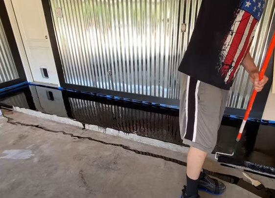 This image shows a man applying epoxy paint on an industrial floor.